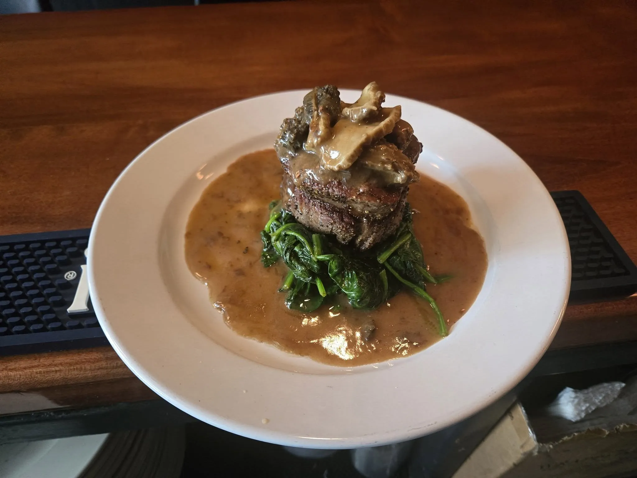A beef filet topped with mushrooms over sautéed spinach in pan sauce.