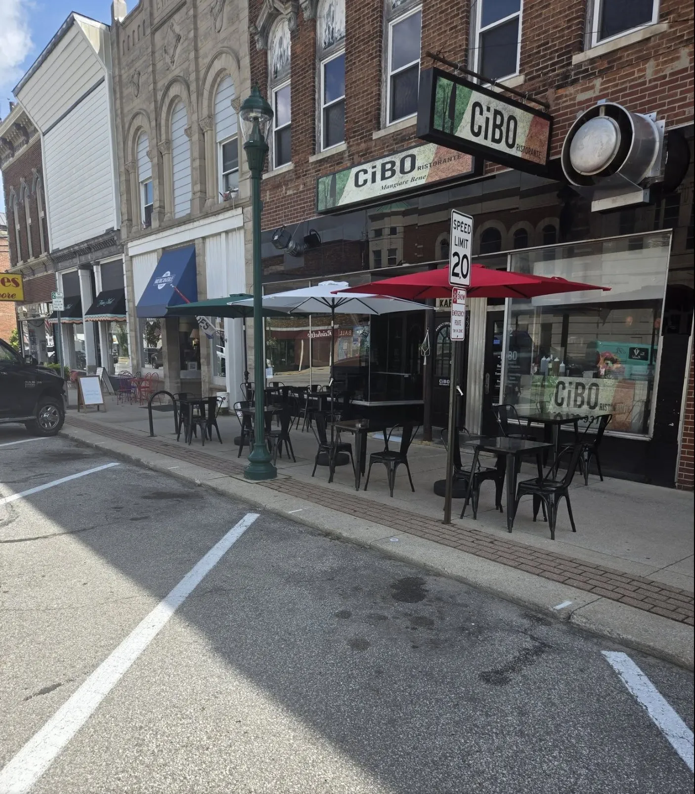 Tables and umbrellas on the sidewalk outside CiBO on West Van Buren Street, with the brick storefronts of downtown Columbia City.