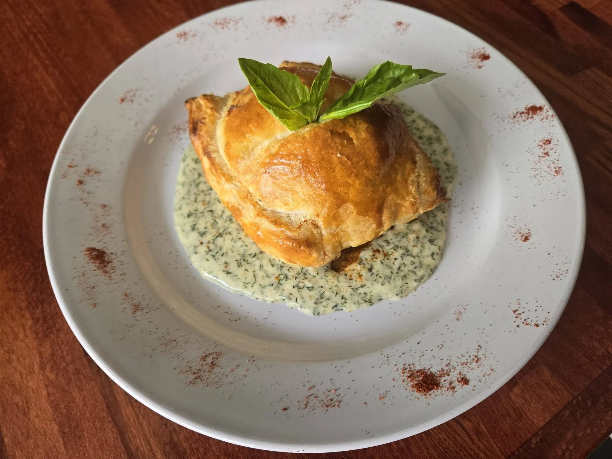 A golden puff pastry parcel on a dill cream sauce, topped with basil.